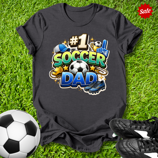 Black t-shirt with '#1 Soccer Dad' design on grass with soccer ball and shoes.