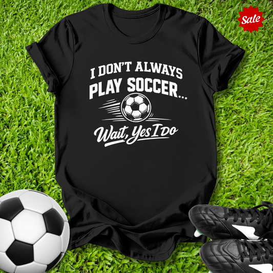 Black t-shirt with soccer-themed text on grass with soccer ball and shoes
