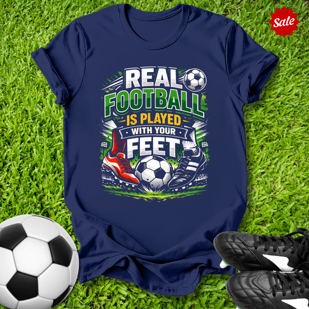 Navy blue t-shirt with soccer-themed design on grass with soccer ball and shoes