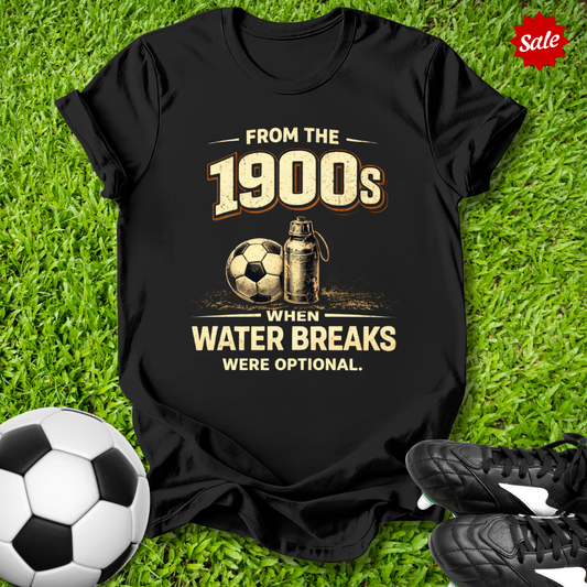 Black t-shirt with vintage soccer design with from the 1900s when water breaks were optional on grass text on grass with soccer ball and shoes