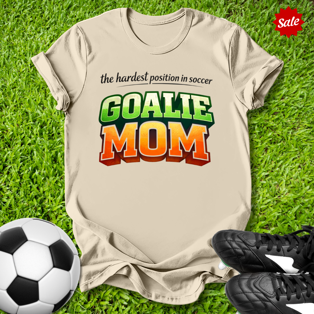 Beige t-shirt with 'GOALIE MOM' text on grass with soccer ball and shoes
