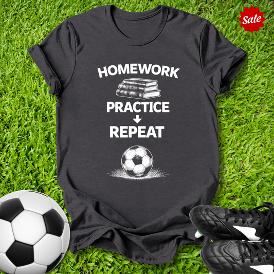 Black t-shirt with 'Homework Practice Repeat' text on grass with soccer balls and shoes.