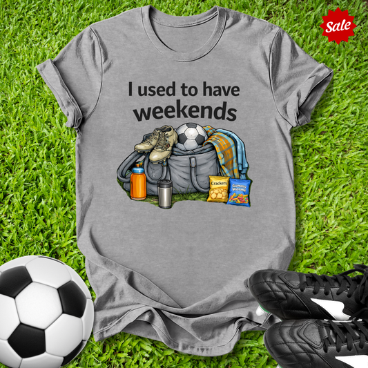 Gray t-shirt with graphic and text on grass with soccer ball and shoes
