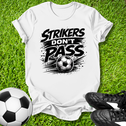 White t-shirt with 'Strikers Don't Pass' graphic on grass with soccer ball and cleats.