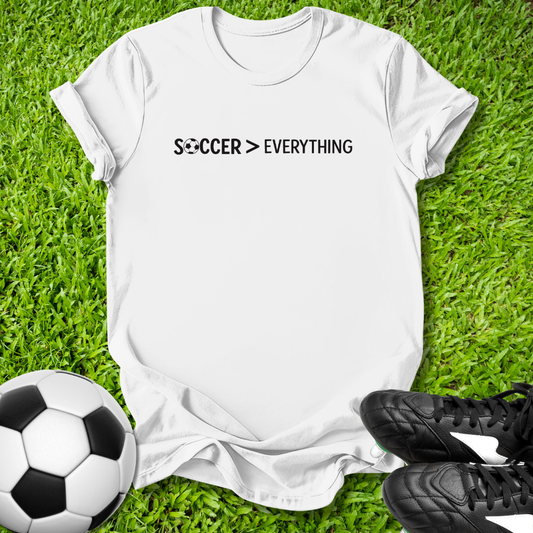 White t-shirt with 'Soccer > Everything' text on grass with soccer ball and shoes.