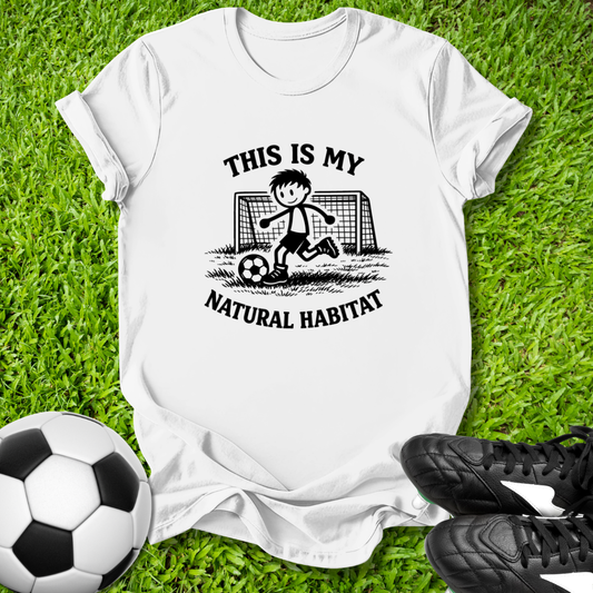 White t-shirt with soccer graphic and this is my natural habitat text on grass with soccer ball and shoes
