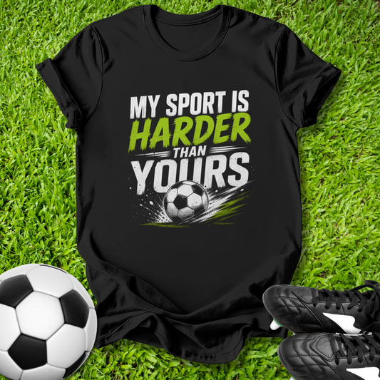 Black t-shirt with 'My sport is harder than yours' text and soccer ball graphic on grass with soccer ball and shoes.