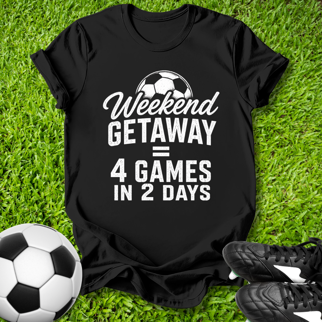 Black t-shirt with 'Weekend Getaway = 4 Games in 2 Days' text on grass with soccer ball and shoes.
