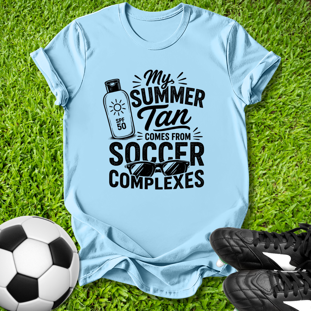 Light blue t-shirt with 'My Summer Tan Comes from Soccer Complexes' text on grass with soccer ball and shoes.