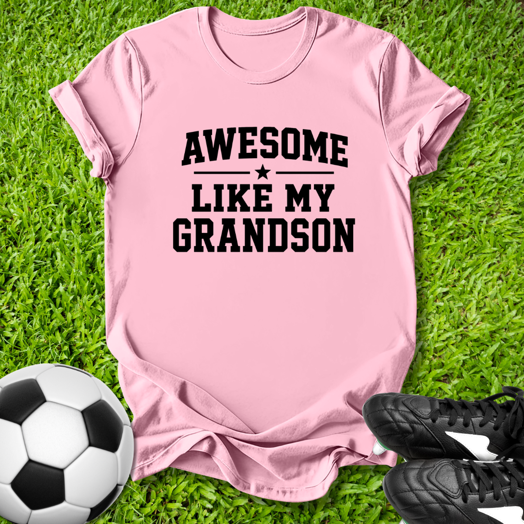 Pink t-shirt with 'Awesome like my grandson' text on grass with soccer ball and shoes.