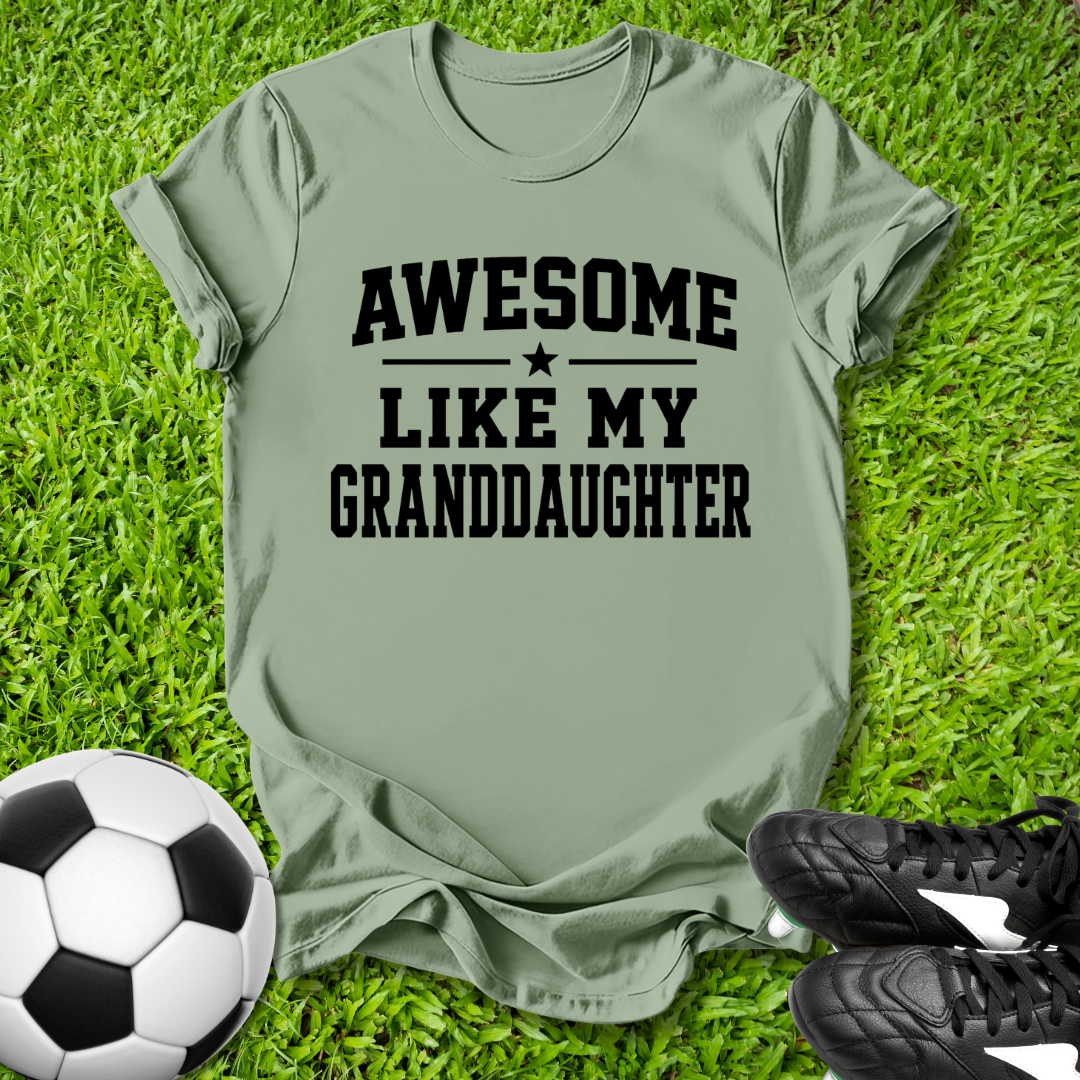 Green t-shirt with 'Awesome Like My Granddaughter' text on grass with soccer ball and shoes.