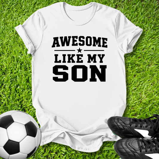 White t-shirt with 'Awesome Like My Son' text on grass with soccer ball and shoes