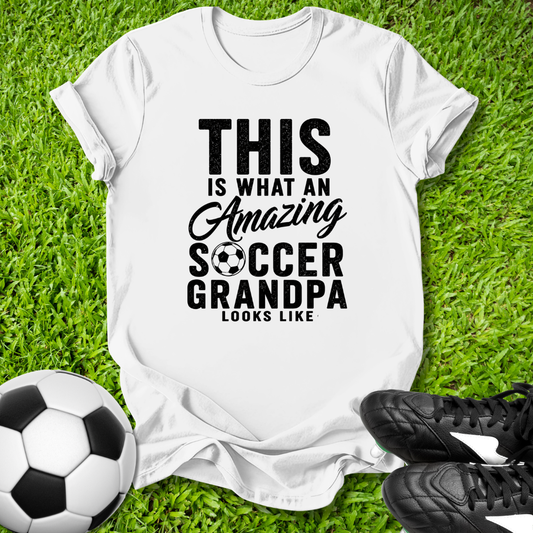 White t-shirt with 'Amazing Soccer Grandpa' text on grass with soccer ball and shoes