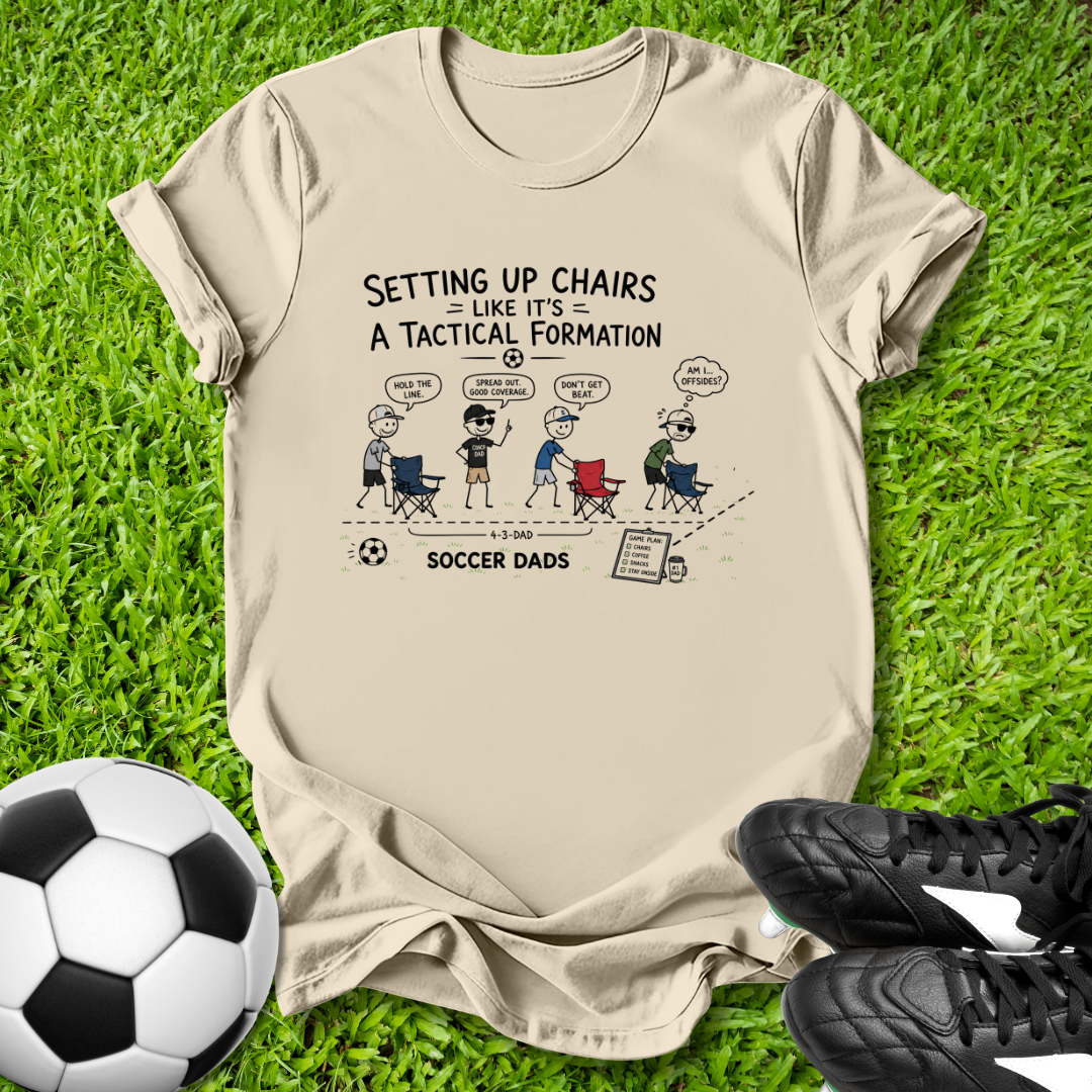 Beige t-shirt with soccer-themed graphic on grass with soccer ball and shoes