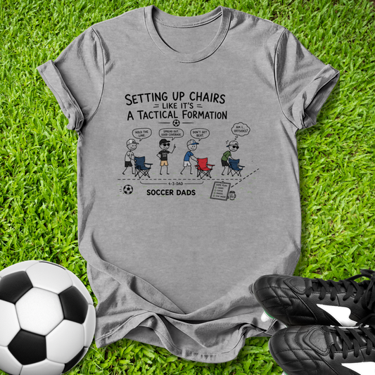 Gray t-shirt with soccer-themed graphic on grass with soccer ball and shoes
