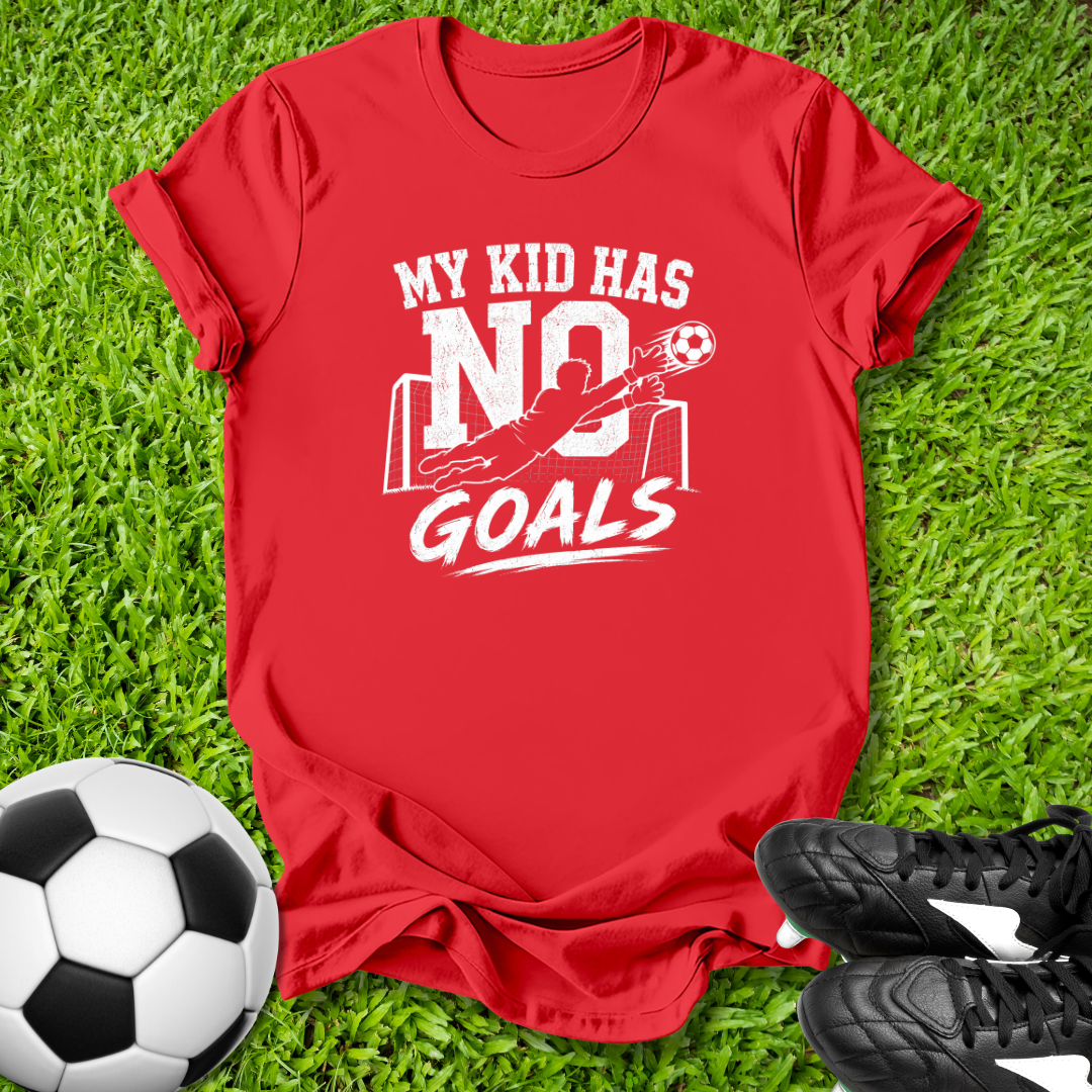 Red t-shirt with 'My kid has no goals' text on grass with soccer ball and shoes.