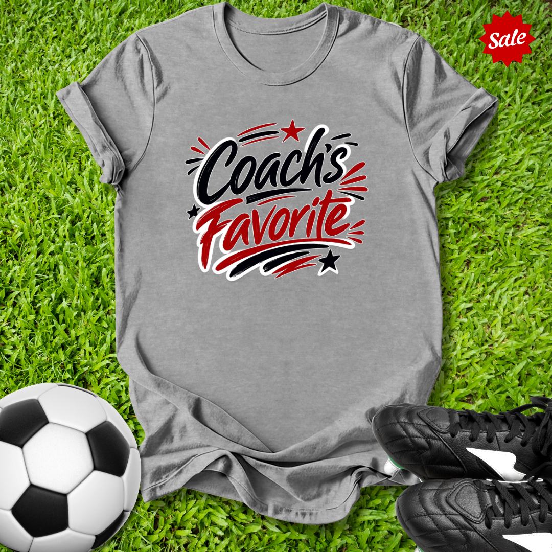 Gray t-shirt with 'Coach's Favorite' text on grass with soccer ball and shoes