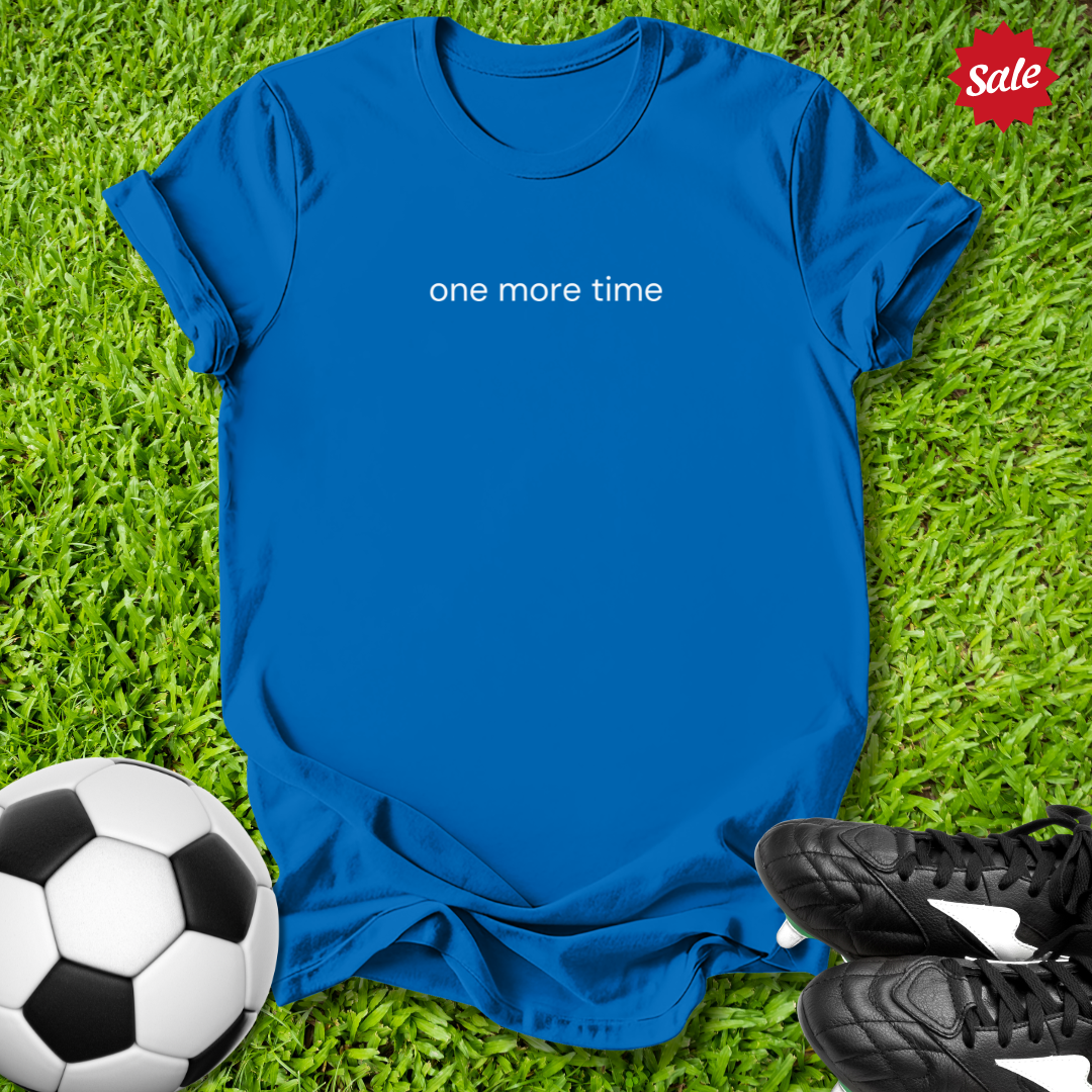 Blue t-shirt with 'one more time' text on grass with soccer ball and shoes