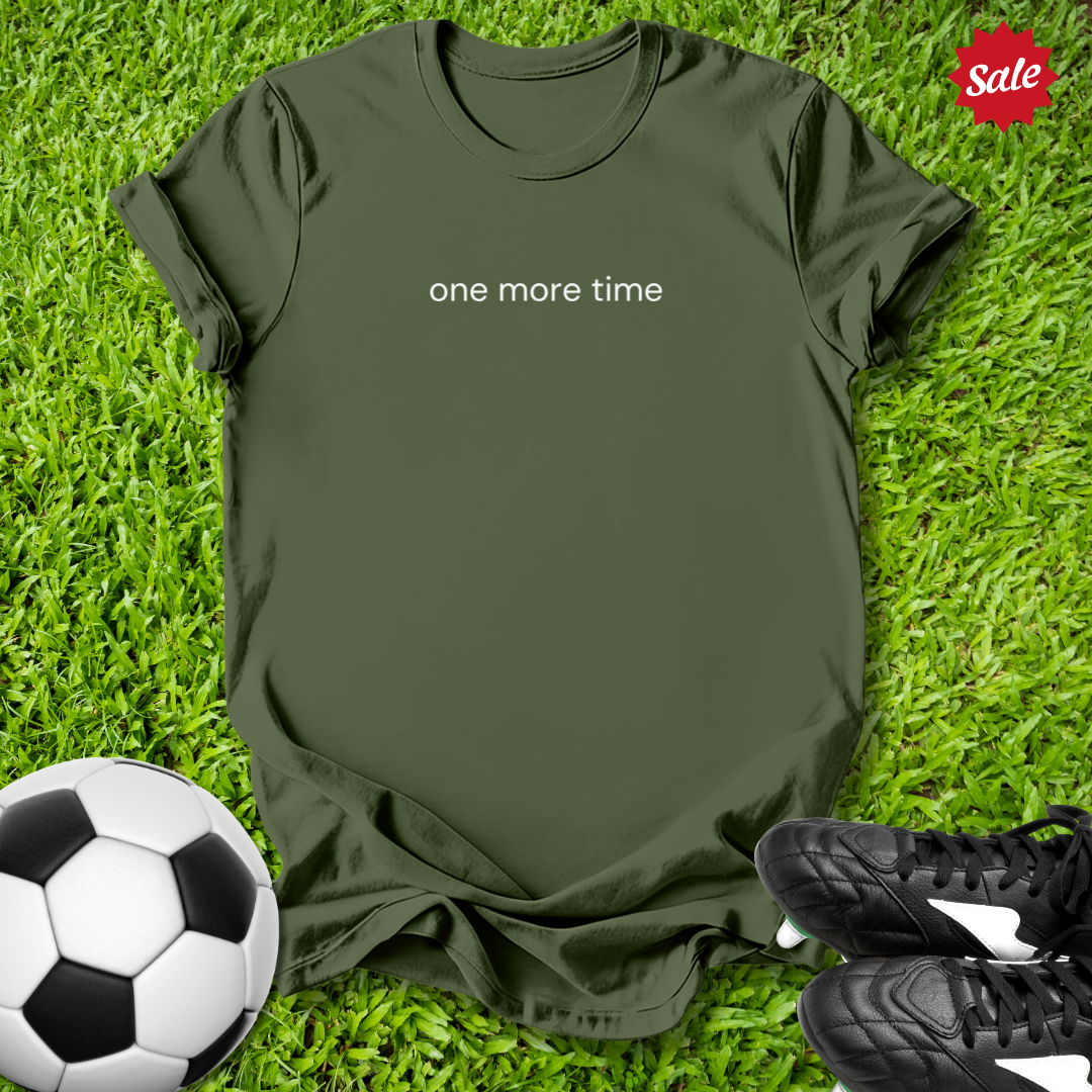 Green t-shirt with 'one more time' text on grass with soccer ball and shoes