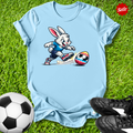 Light blue t-shirt with  the  Easter bunny playing soccer on grass with soccer balls and shoes.