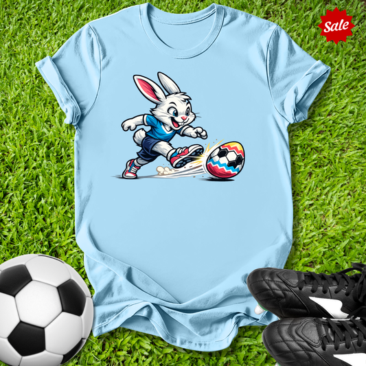Light blue t-shirt with  the  Easter bunny playing soccer on grass with soccer balls and shoes.