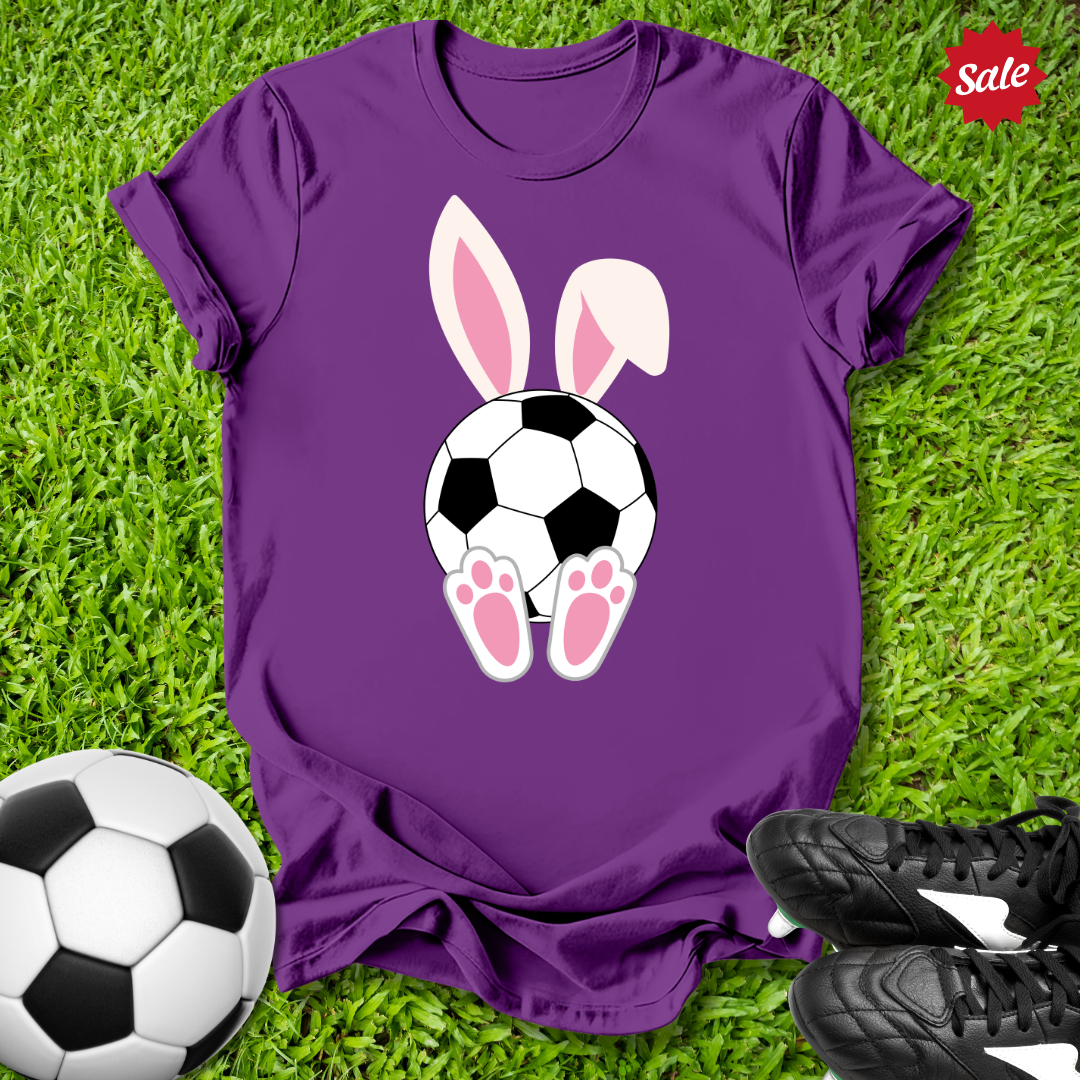 Purple t-shirt with  Easter bunny ears and soccer ball design on grass with soccer ball and shoes.