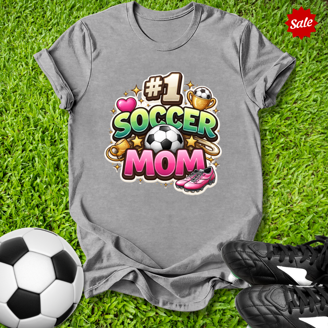 Gray t-shirt with '#1 Soccer Mom' design on grass with soccer ball and shoes.
