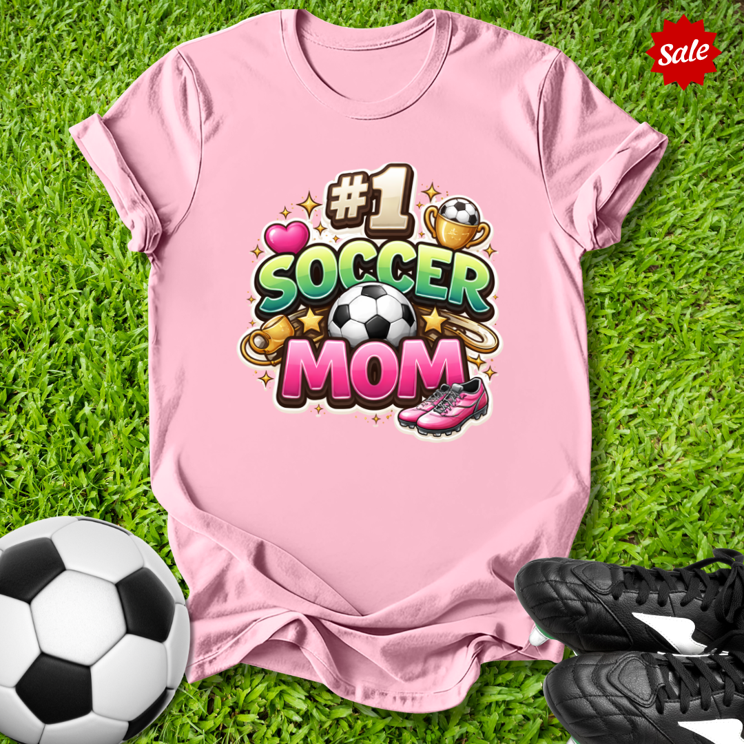 Pink t-shirt with '#1 Soccer Mom' design on grass with soccer ball and shoes