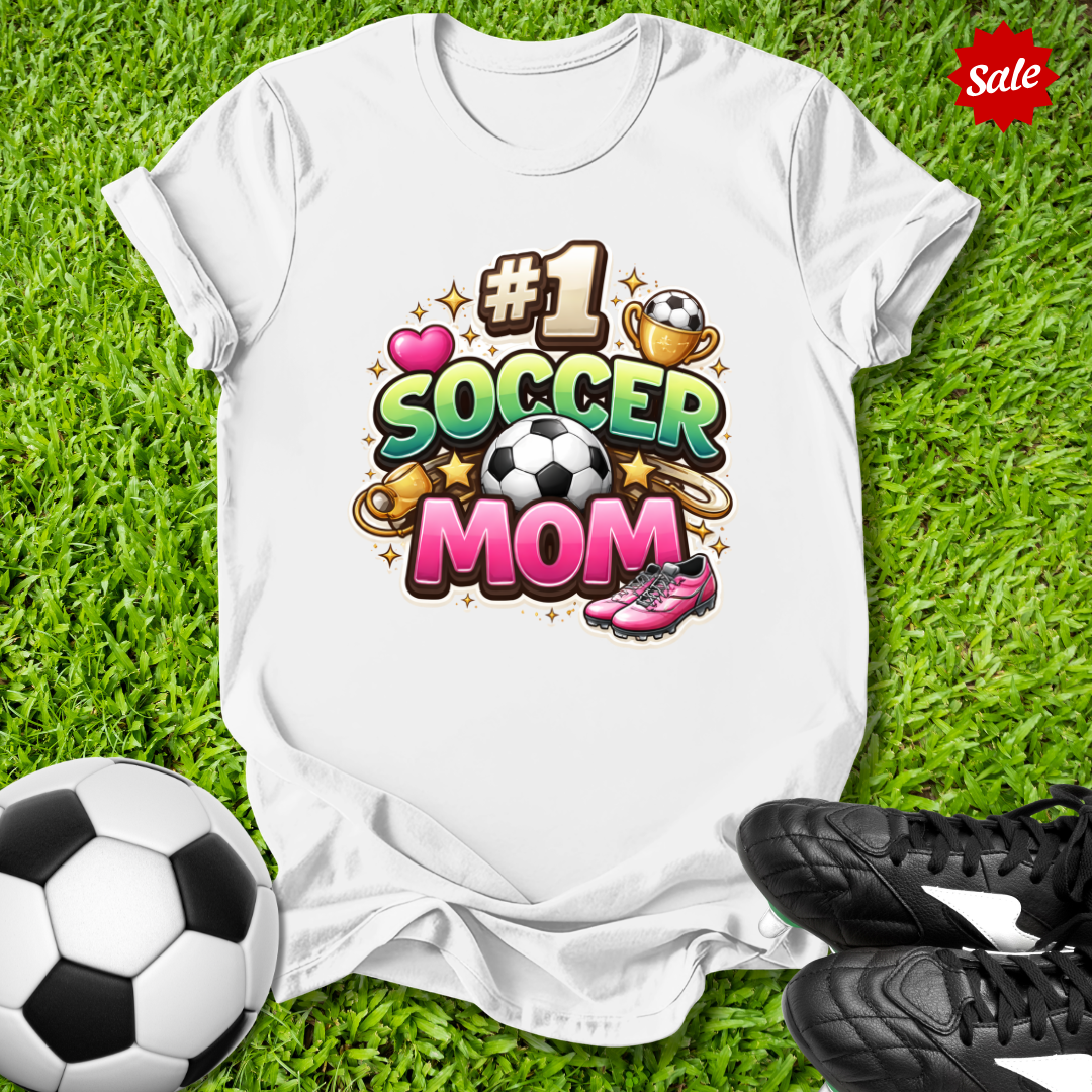 White t-shirt with '#1 Soccer Mom' design on grass with soccer ball and shoes