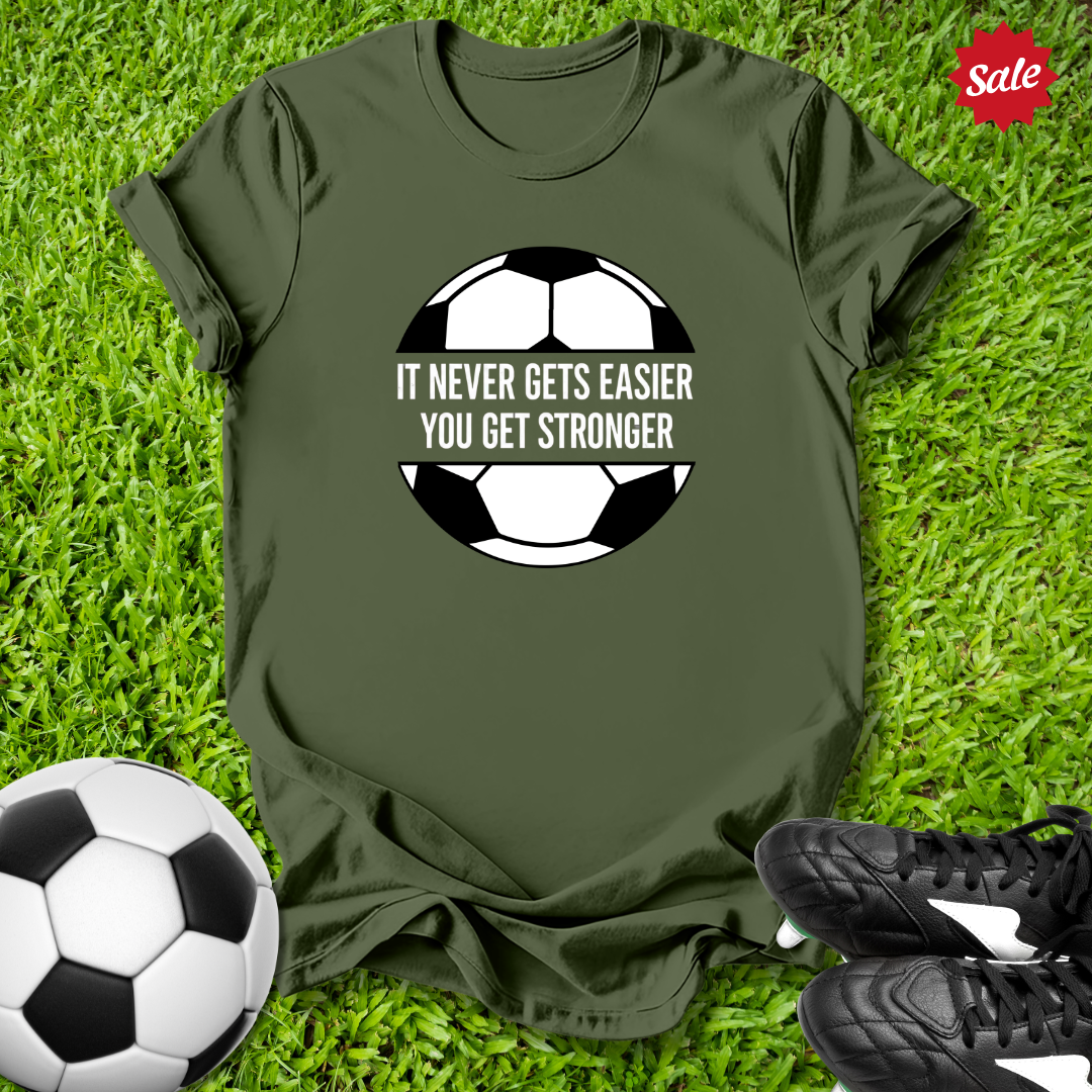 Green t-shirt with motivational quote on a grass background with soccer ball and shoes.
