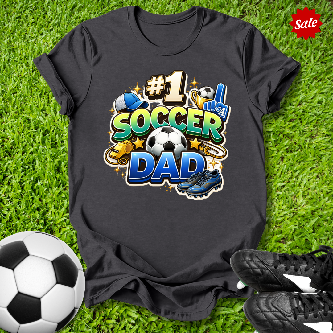Black t-shirt with '#1 Soccer Dad' design on grass with soccer ball and shoes.