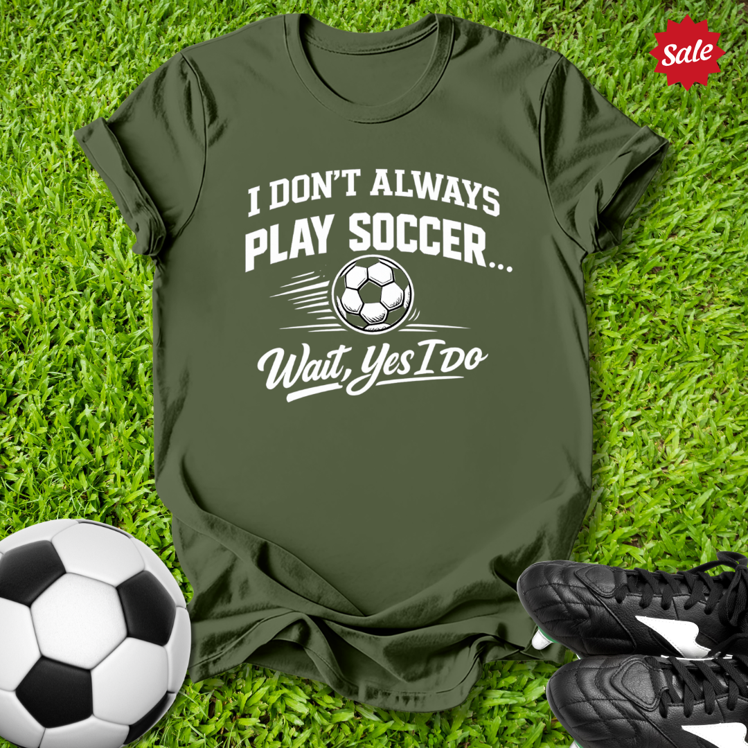 Green t-shirt with soccer-themed text on grass with soccer ball and shoes