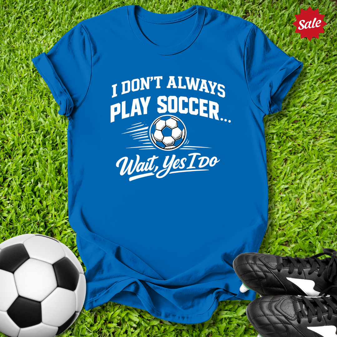 Blue t-shirt with soccer-themed text on grass with soccer ball and shoes