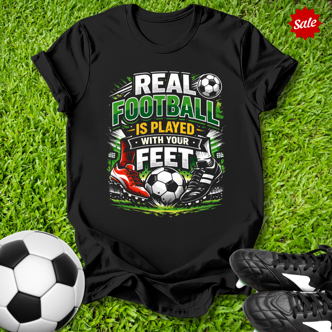 Black t-shirt with soccer-themed design on grass with soccer ball and shoes