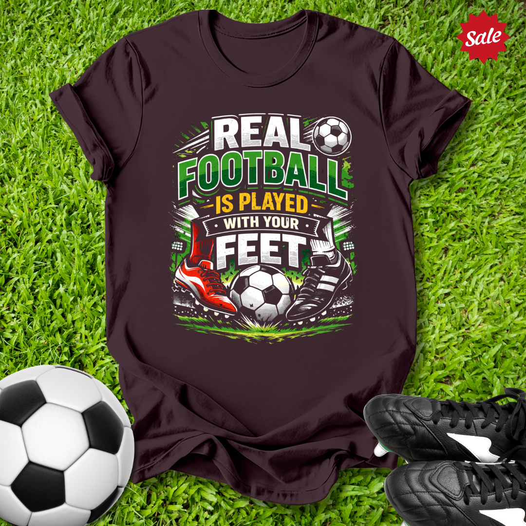 Brown t-shirt with soccer-themed design on grass with soccer ball and shoes