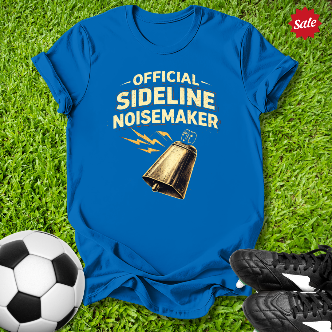 Blue t-shirt with 'Official Sideline Noisemaker' text and bell graphic on grass with soccer ball and shoes.