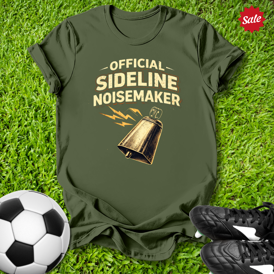 Green t-shirt with 'Official Sideline Noisemaker' design on grass with soccer ball and shoes.
