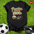 Black t-shirt with 'Practice like it's the 1900s' design on grass with soccer ball and shoes.