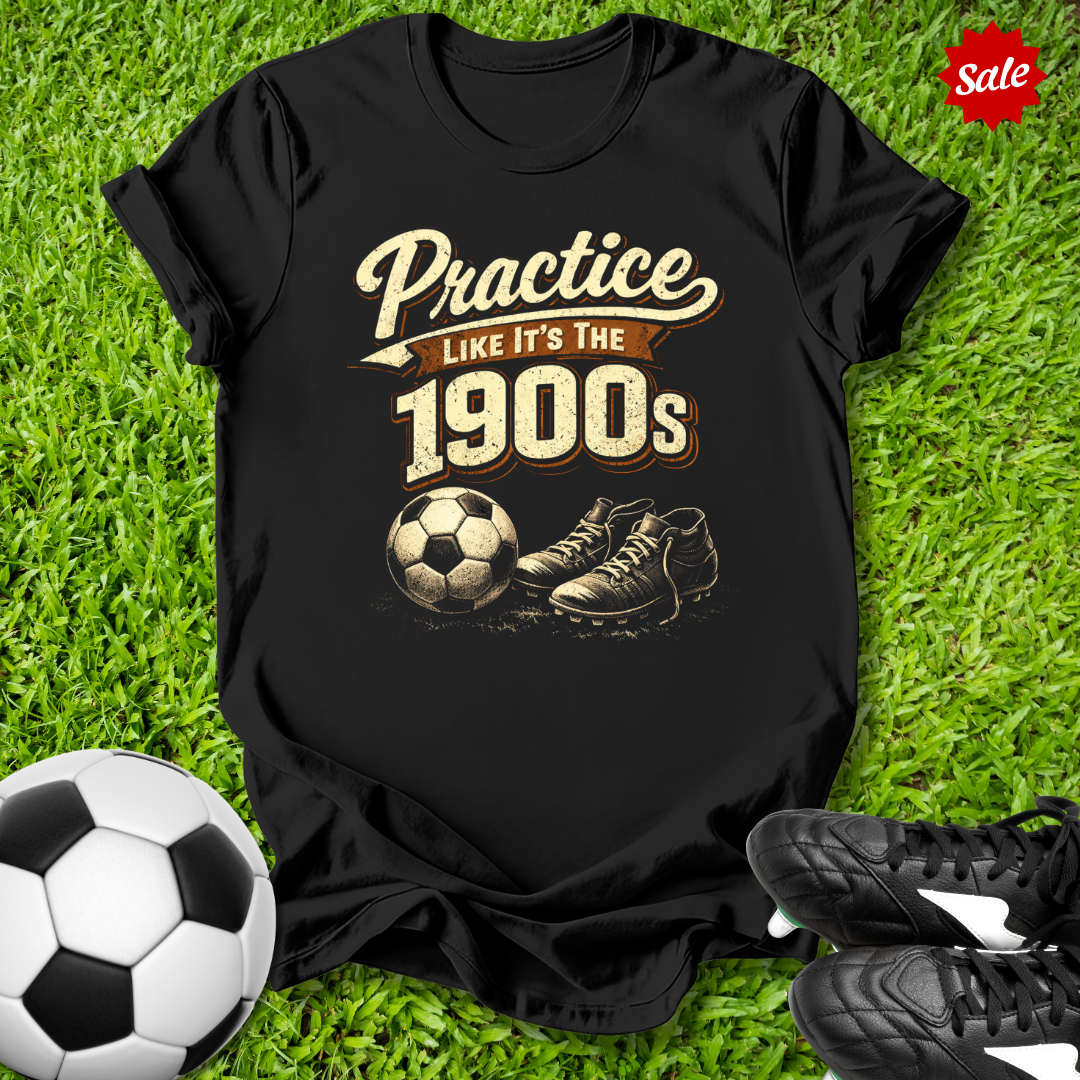 Black t-shirt with 'Practice like it's the 1900s' design on grass with soccer ball and shoes.