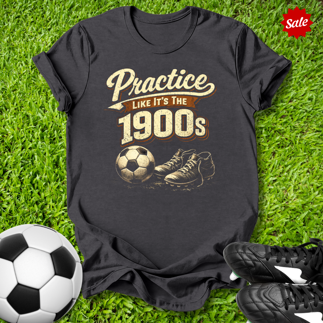 Black t-shirt with 'Practice like it's the 1900s' design on grass with soccer ball and shoes.