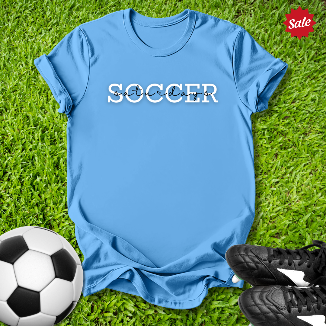 Blue t-shirt with 'Soccer Saturdays' text on grass with soccer ball and shoes