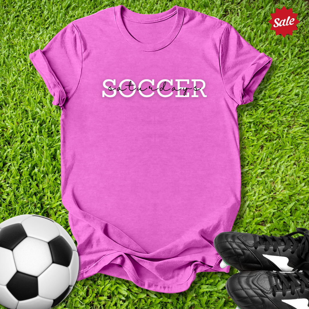 Pink t-shirt with 'Soccer Saturdays' text on grass with soccer ball and shoes