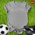 Gray t-shirt with 'Soccer Saturdays' text on grass with soccer ball and shoes