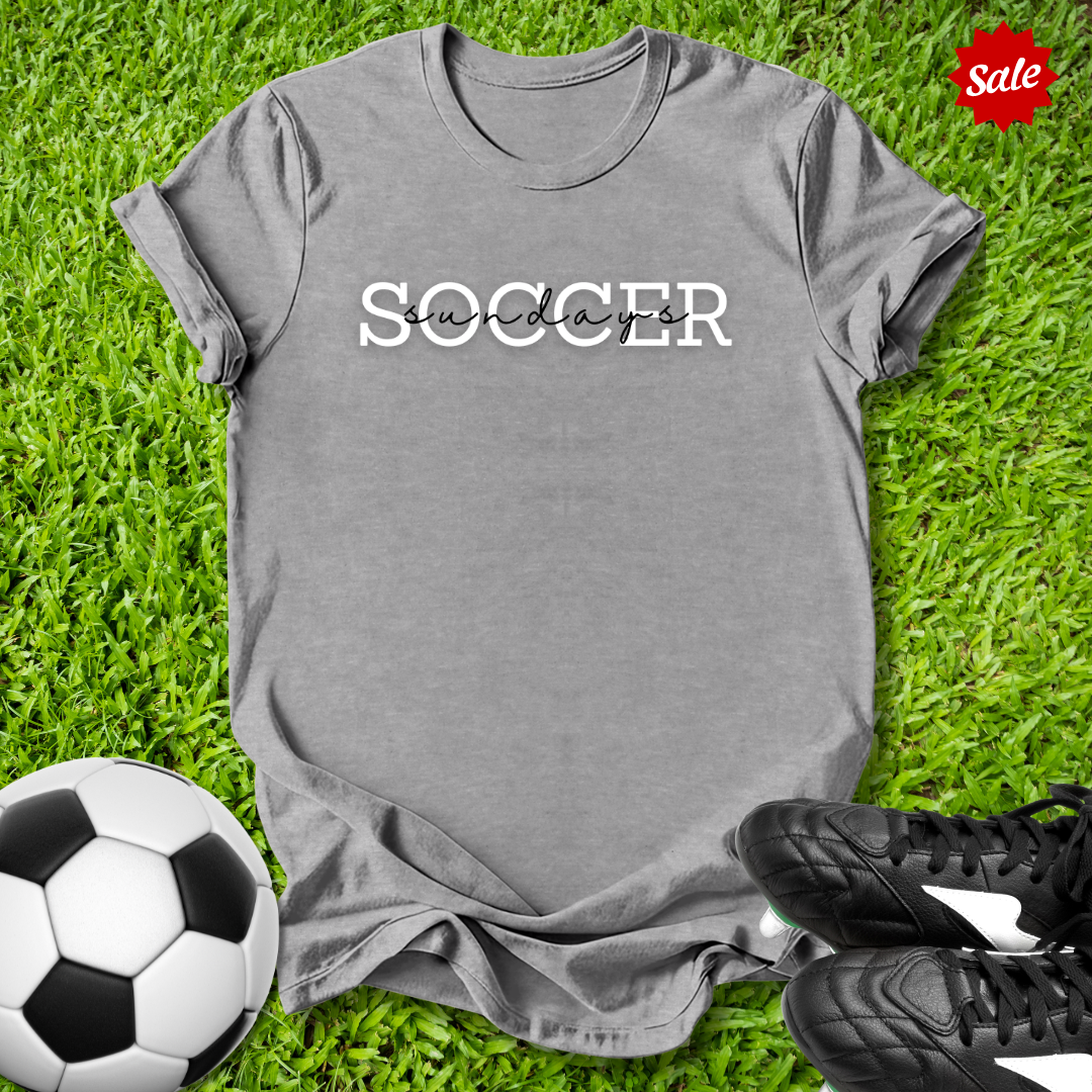 Gray t-shirt with 'Soccer Saturdays' text on grass with soccer ball and shoes