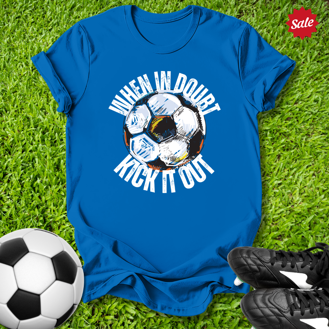 Blue t-shirt with when in doubt kick it out soccer ball graphic and text on grass with soccer ball and shoes