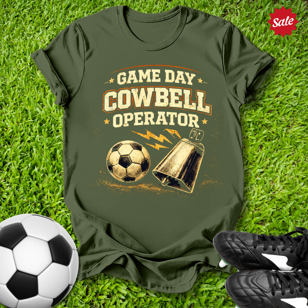 Green t-shirt with 'Game Day Cowbell Operator' design on grass with soccer ball and shoes.
