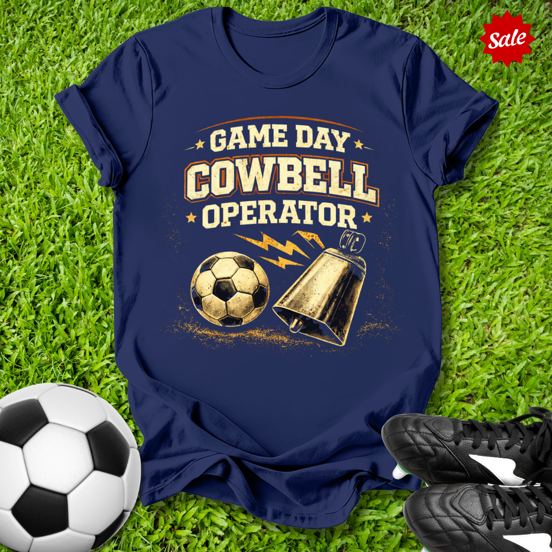 Navy blue t-shirt with 'Game Day Cowbell Operator' design on grass with soccer ball and shoes.
