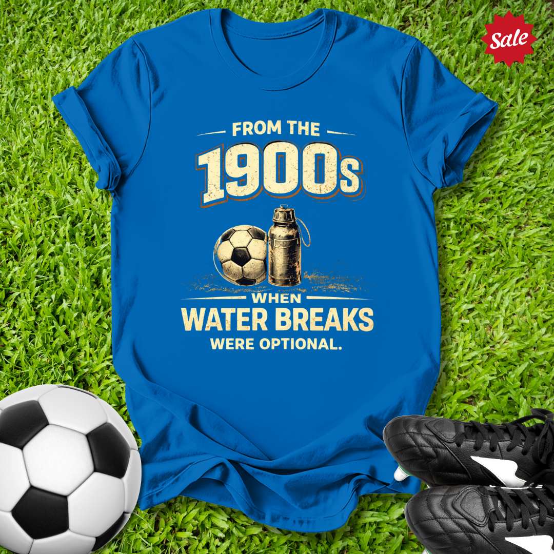 Blue t-shirt with vintage soccer design with from the 1900s when water breaks were optional on grass  text  on grass with soccer ball and shoes