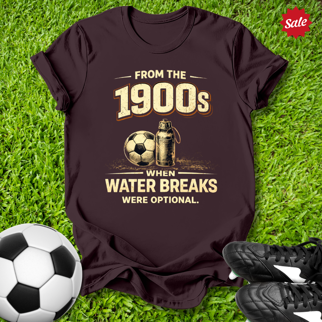 Brown t-shirt with vintage soccer design on grass with from the 1900s when water breaks were optional on grass  text  with soccer ball and shoes