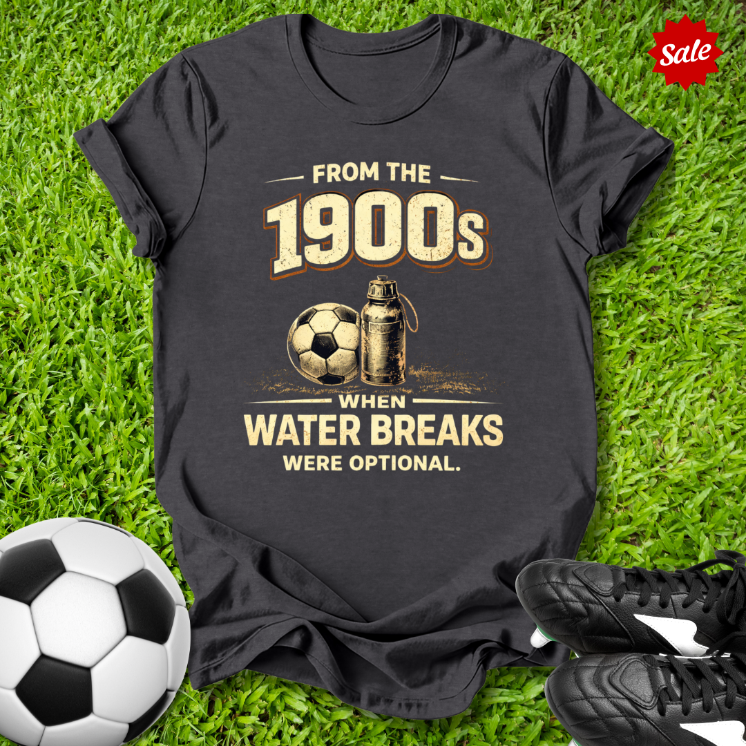 Black t-shirt with vintage soccer design with from the 1900s when water breaks were optional on grass  text  on grass with soccer ball and shoes